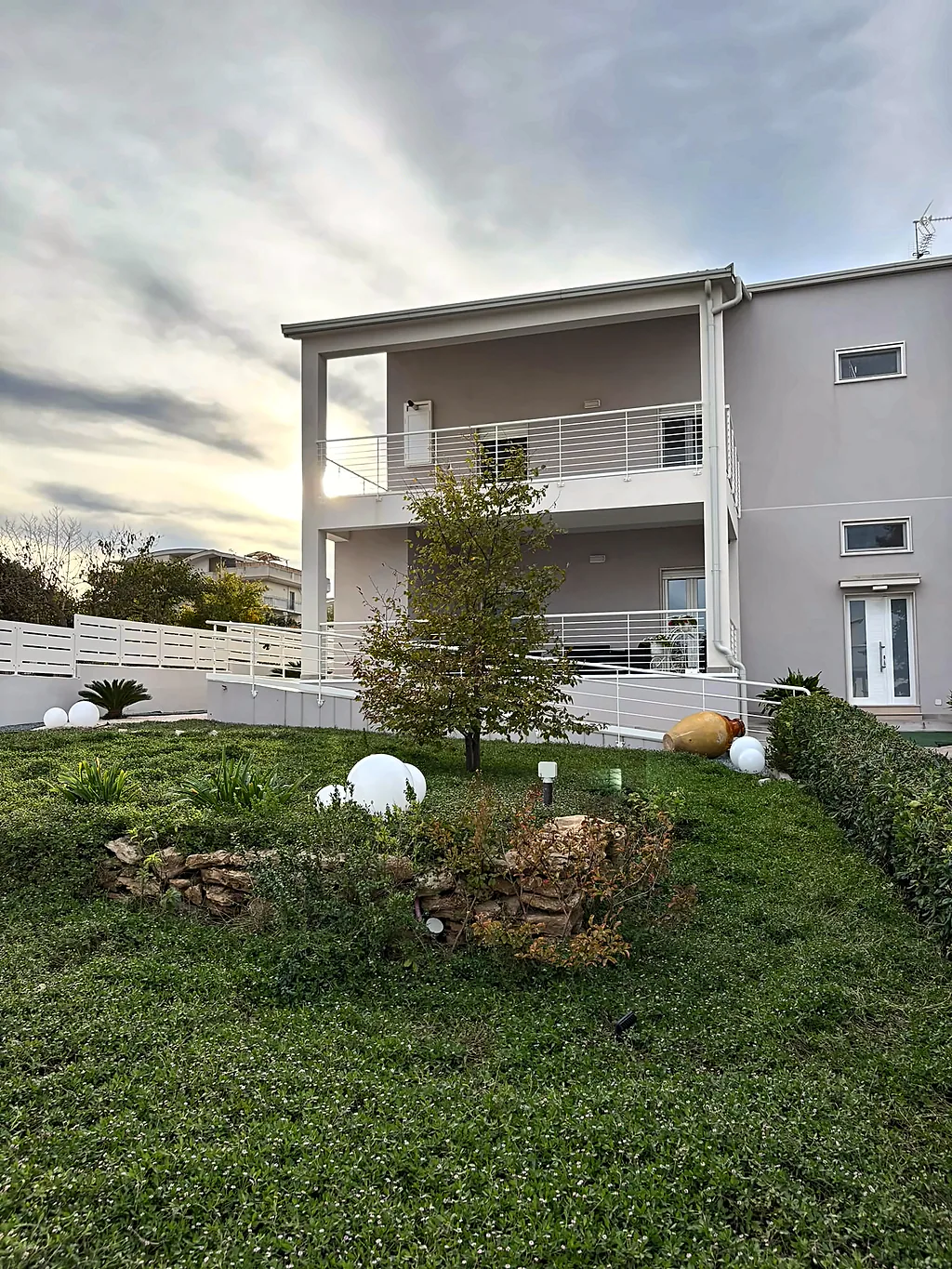 La casa vista dal giardino: una betulla, l'aiuola con pietre, le lampade a sfera e le siepi ai lati del prato