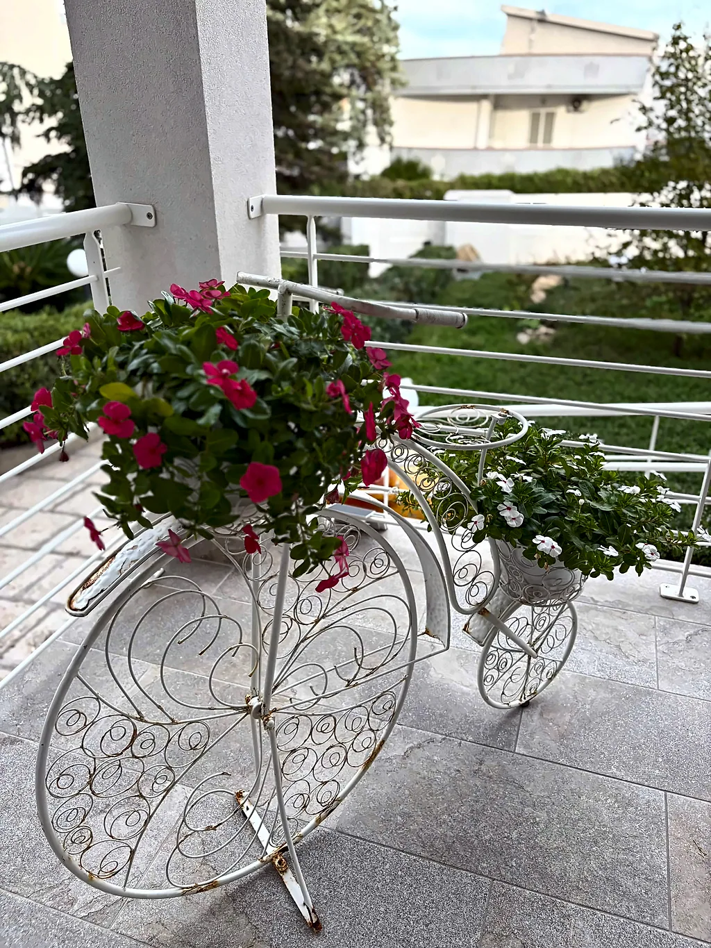 Una bicicletta decorativa in ferro bianco con vasi di fiori rossi e bianchi